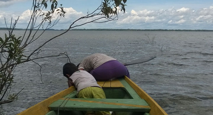 Eliana und ihr Cousim Lucas holen Netze aus dem See. Auf der linken Seite ragen überflutete Sträucher ins Bild.