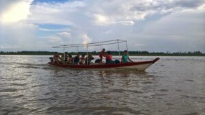 Ein kleines Boot fährt mit 11 Personen in der Mitte eines Flusses, der mehrere hundert Meer breit ist.